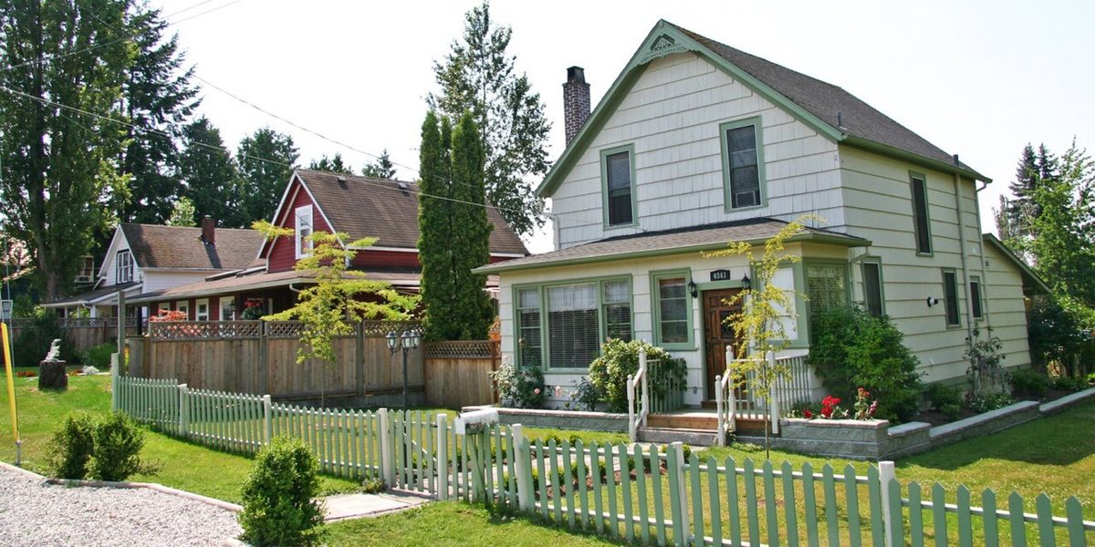 A quiet residential street in Murrayville with an older two-storey white house, a picket fence, gardens and tall trees