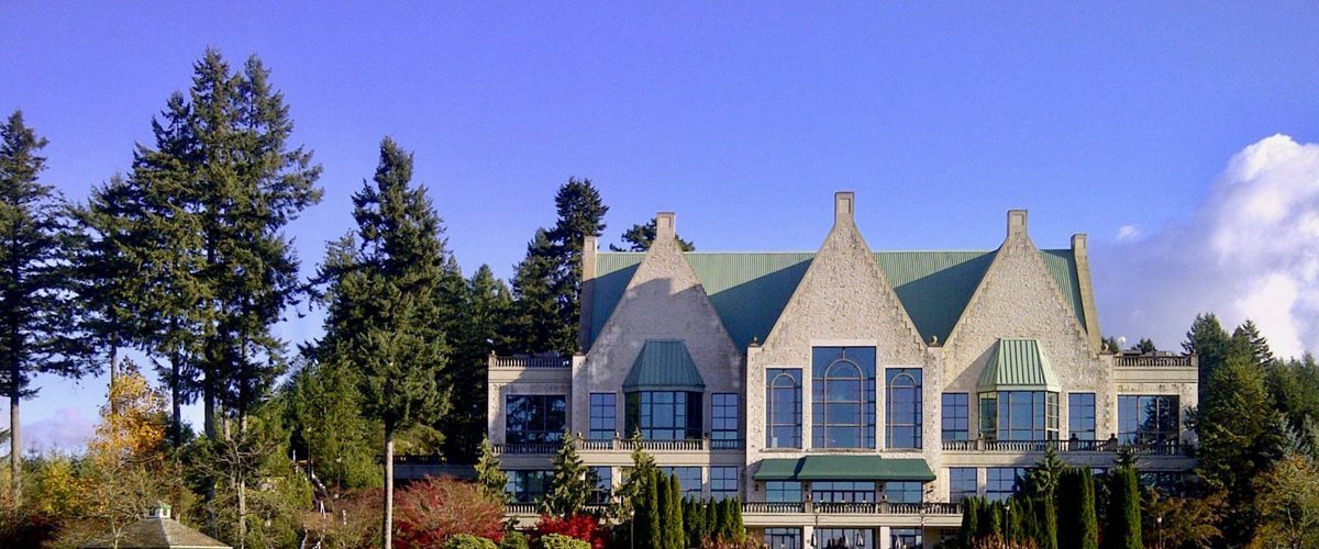 The stone, chateau-style clubhouse at Swaneset Bay, seen across a green with tall evergreens behind