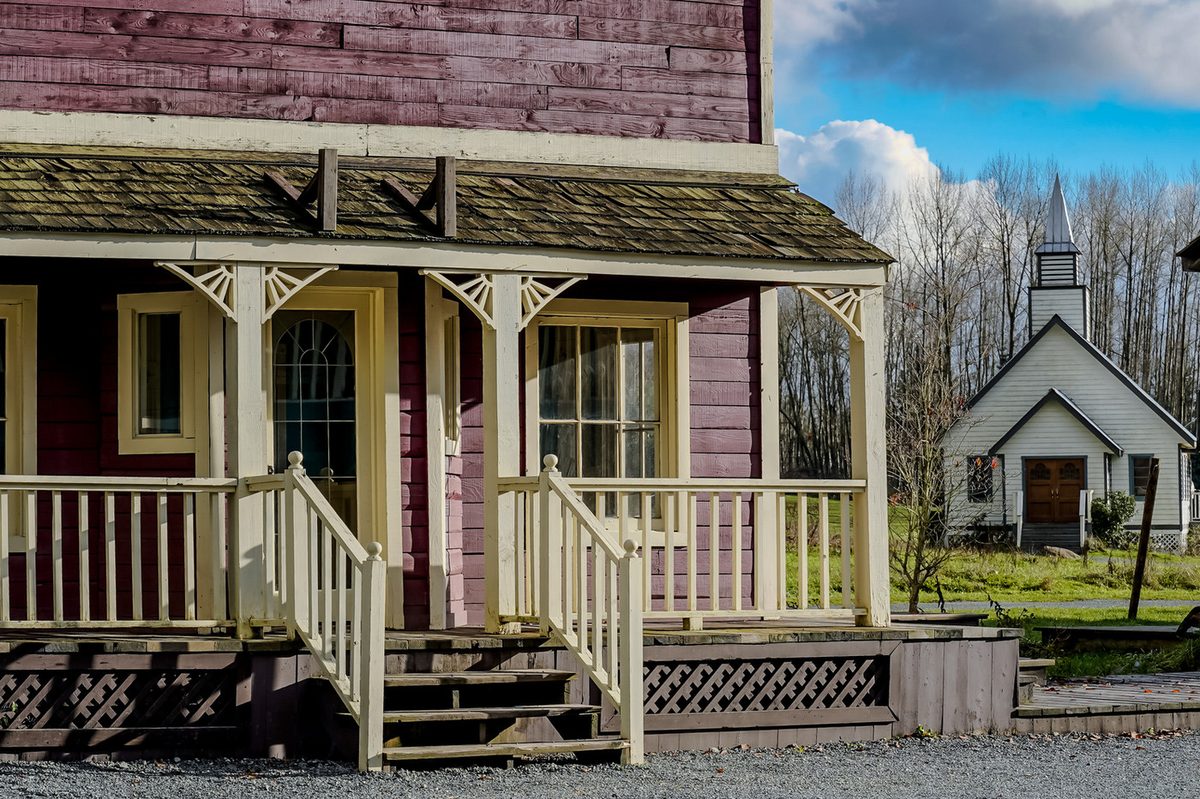 A porch on the Jamestown set with a small white church with a steeple behind it
