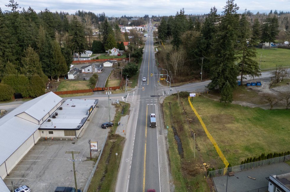 Aerial view of Fraser Highway during the Township's widening project, a road lined by a warehouse, houses, trees and farmland