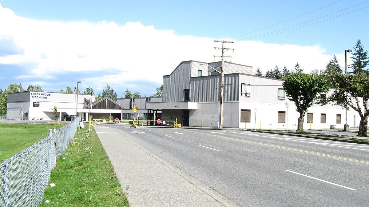 The front of Brookswood Secondary School on 37A Avenue, with the main entrance, a sidewalk and the school field behind a fence