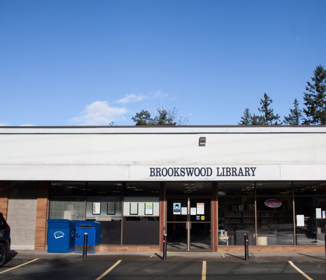 The storefront of Brookswood Library in the shopping strip on 40 Avenue, with blue Canada Post boxes beside the door