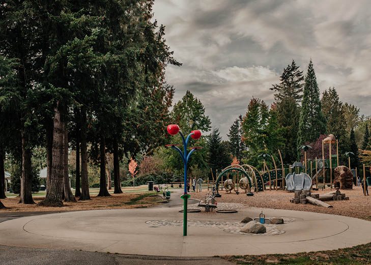 The spray park and playground at City Park in Langley City, ringed by tall evergreen trees