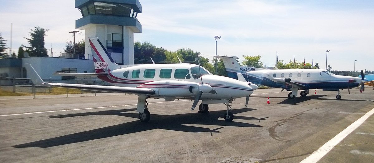 Two small passenger aircraft parked on the apron in front of the control tower at Langley Regional Airport on 216 Street