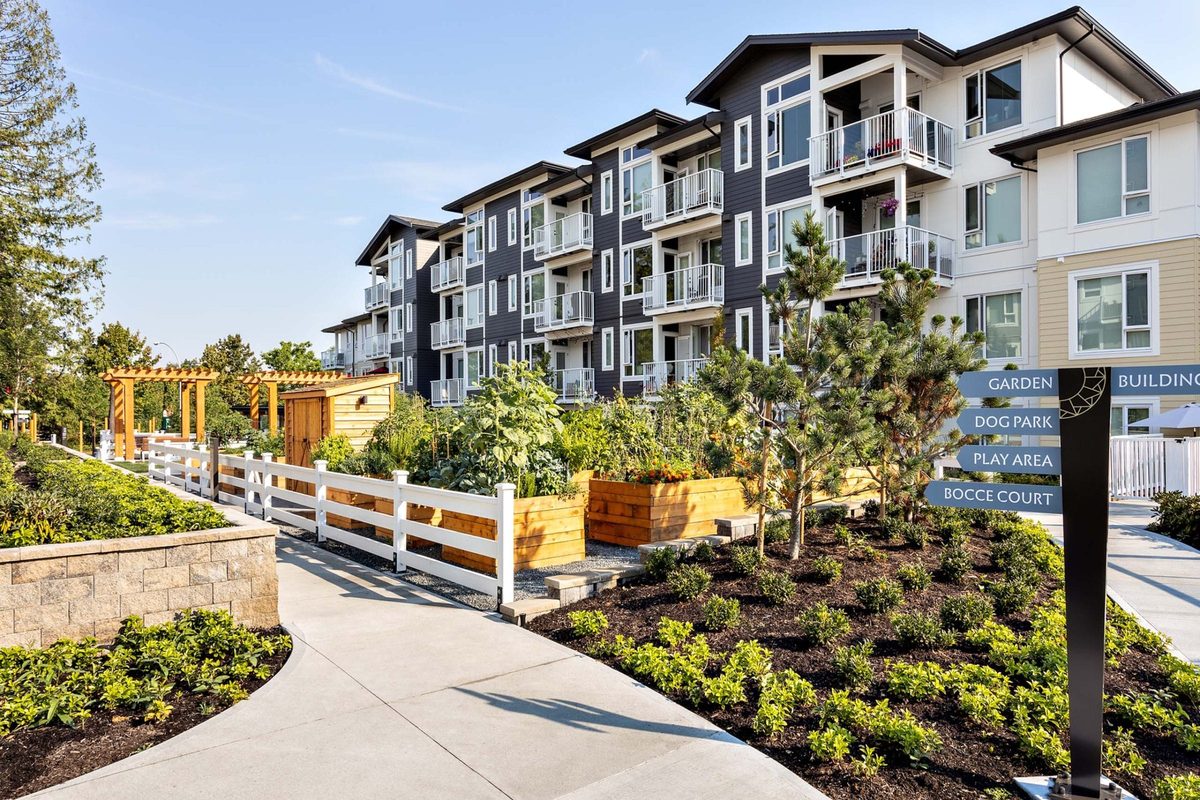 A four-storey apartment building with balconies behind raised garden beds and a sign pointing to the garden, dog park, play area and bocce court, at Solaro in Murrayville