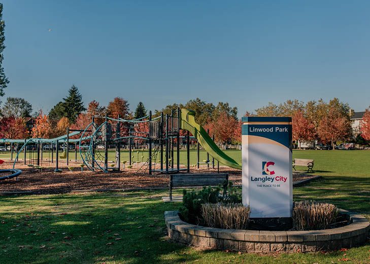The playground and Linwood Park sign at Linwood Park on 201A Street, with climbing structures, open grass and autumn trees behind
