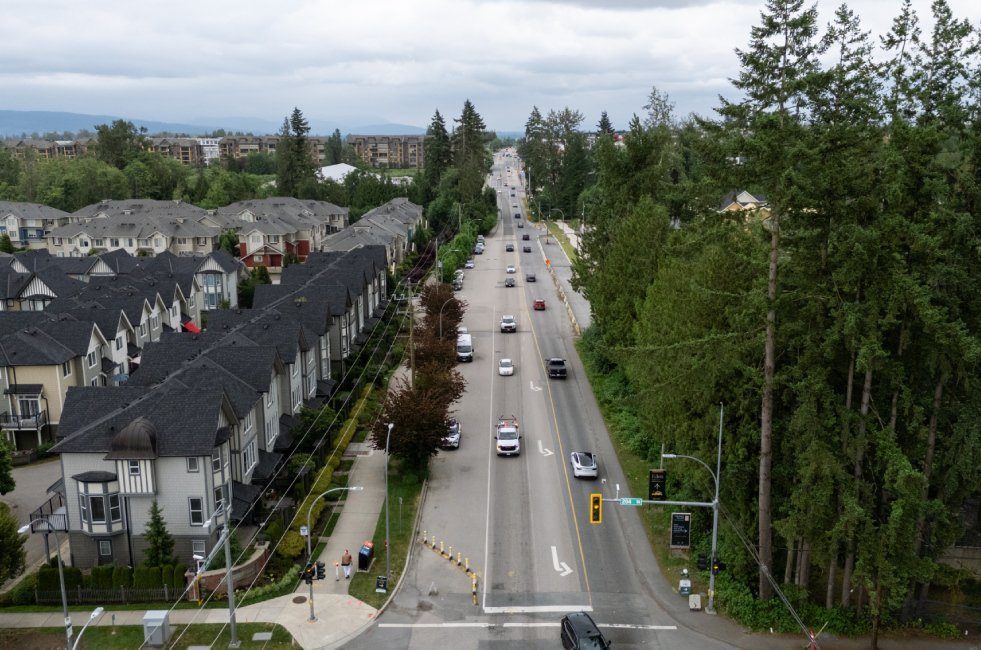 Aerial view along 80 Avenue in Yorkson at 204 Street, with rows of grey townhouses on the left, a four-lane road in the middle and tall evergreens on the right