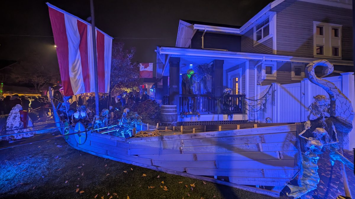 A full-size Viking longship with a striped sail on a front lawn, lit blue, with a house behind it