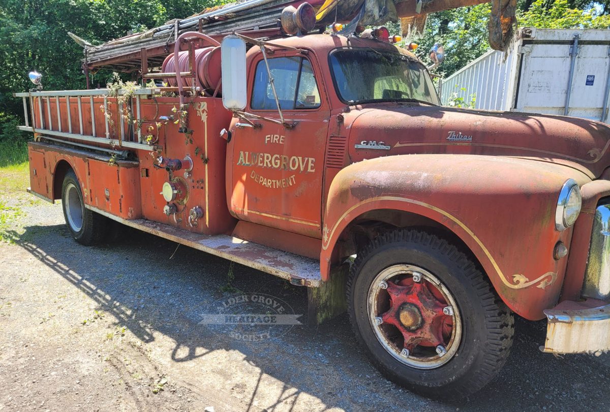 A faded red 1954 GMC fire pumper with Aldergrove Fire Department lettering on the door