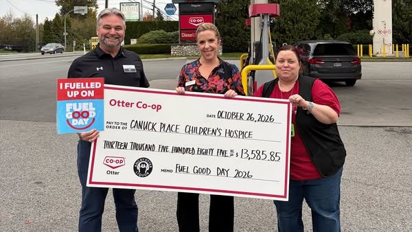 Three people under a Co-op gas bar canopy holding an oversized cheque from Otter Co-op to Canuck Place Children's Hospice for $13,585.85, dated October 26, 2026, memo Fuel Good Day 2026