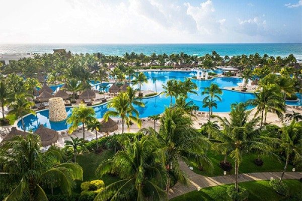 Aerial view of a beach resort in Mexico: palm trees, winding blue pools and thatched umbrellas, with the Caribbean behind