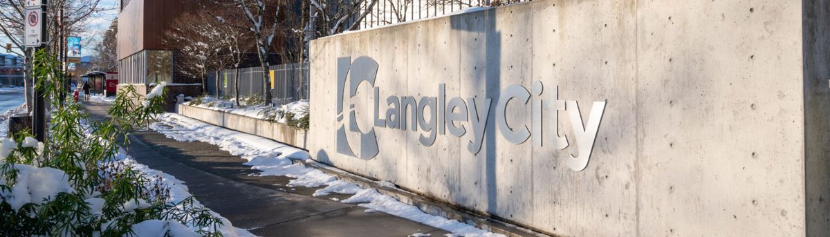 The Langley City sign on a concrete wall downtown, with fresh snow along the sidewalk and planters